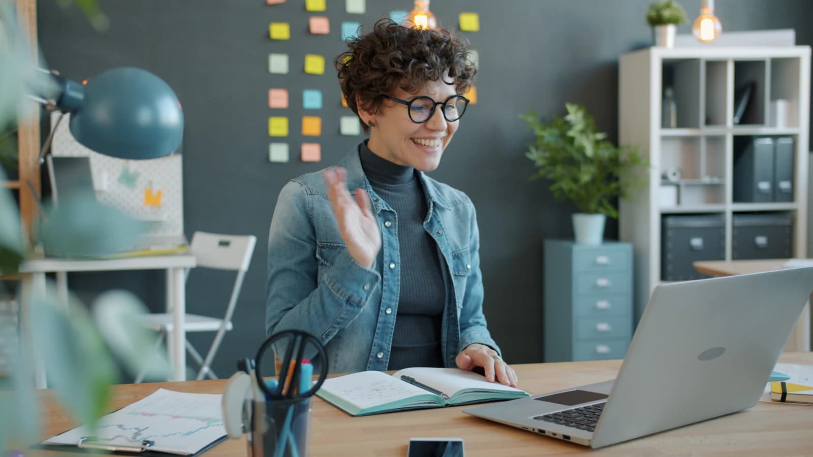 Product designer waving during a live video call in a creative studio