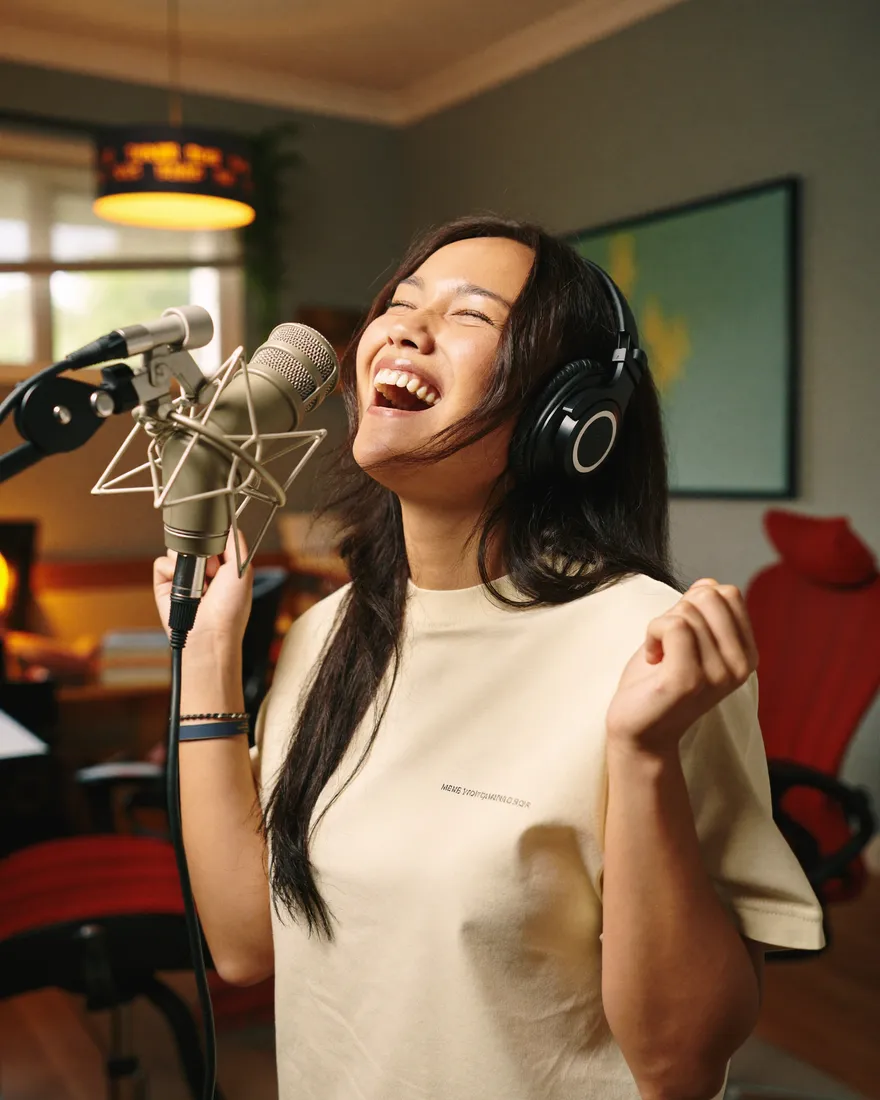 A creator singing into a studio microphone while wearing headphones