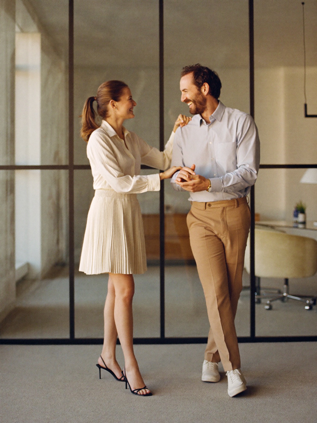 Two professionals collaborating and smiling in a modern glass-walled office